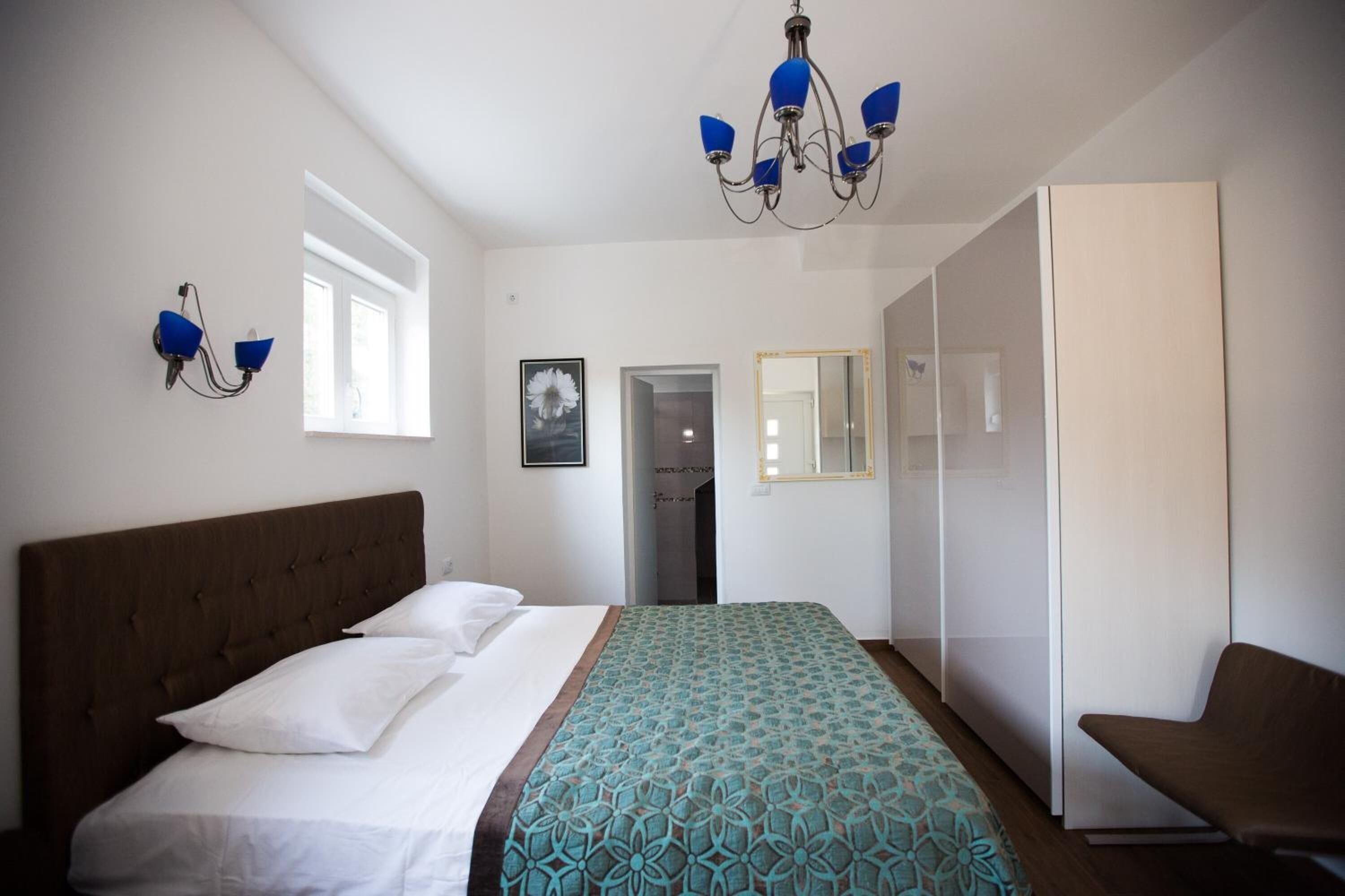 Quarto com cama, lustre, guarda-roupa e porta para outro cômodo.