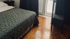 Un dormitorio con cama, mesita de noche, una silla y ventana con cortinas.