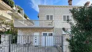 Un edificio de dos pisos con fachada de piedra, un balcón en el piso superior y una entrada con reja.