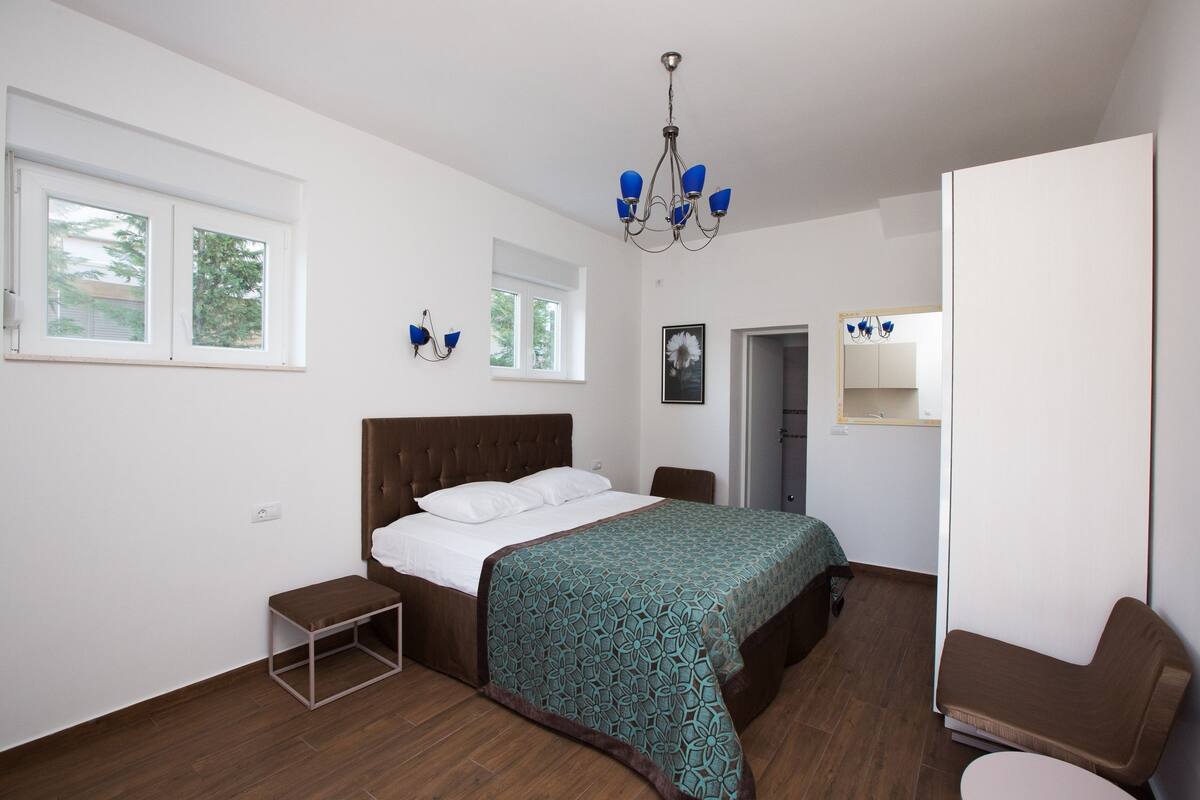 A bedroom with a bed, bedside table, chair, wardrobe, and a chandelier.