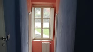 A hallway with a checkered floor, a window with a view of the outside, and a radiator on the wall. - B&B Principe Calaf 4 (Lucca)