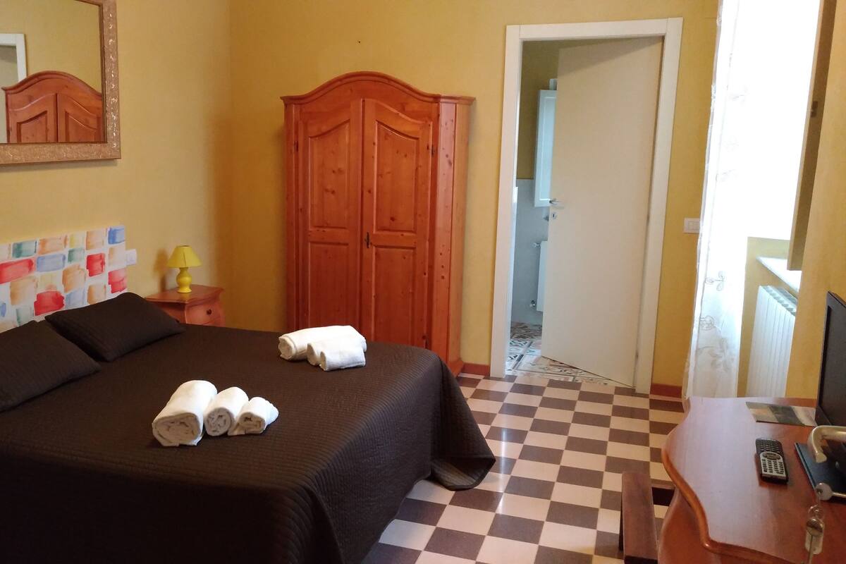 A hotel room with a bed, a wooden wardrobe, a bedside table with a lamp, and a checkered floor.