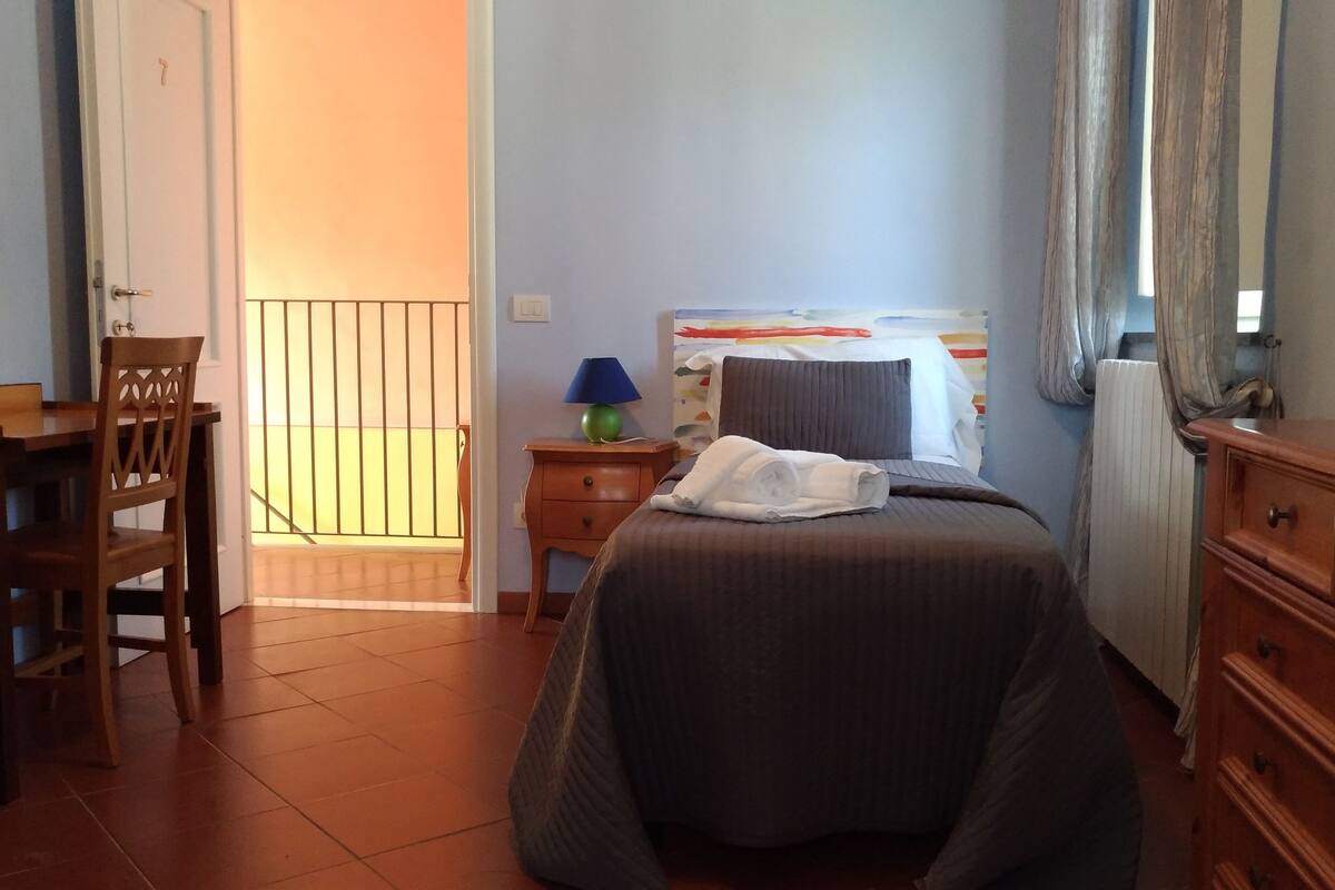 A bedroom with a bed, a nightstand, a lamp, a chair, a dresser, and a door leading to a balcony.