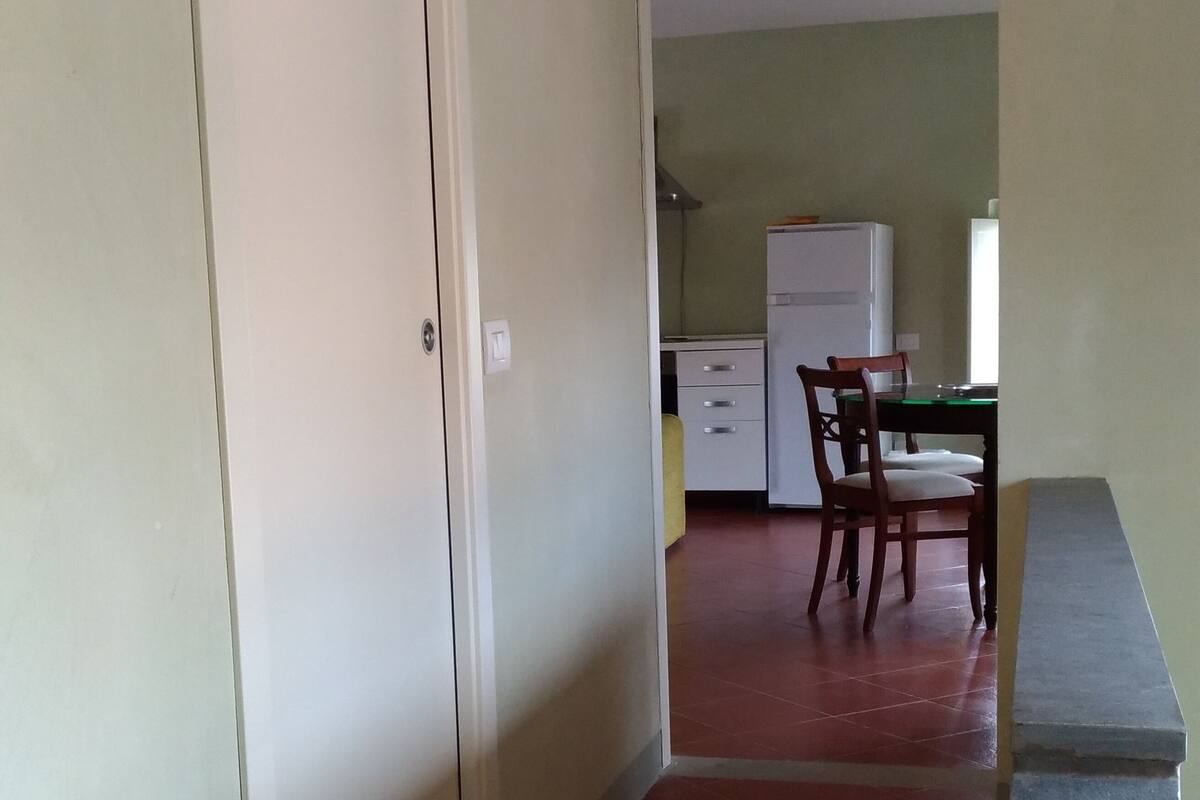 A small, open-plan living area with a kitchenette, a dining table with chairs, and a sliding door leading to another room.