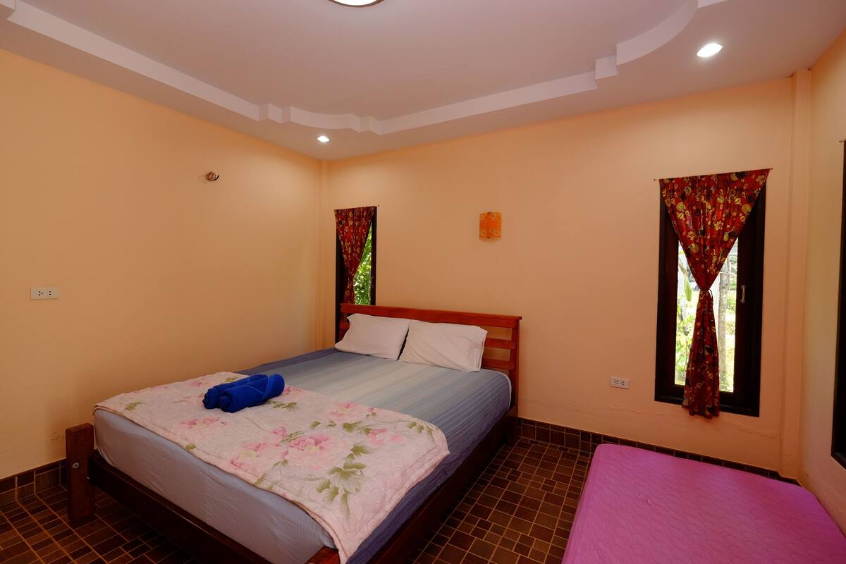 A bedroom with a bed, a bedside table, a window with curtains, and a tiled floor.
