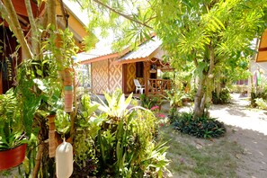 Un jardin tropical avec différentes espèces de plantes et une petite construction en bois.