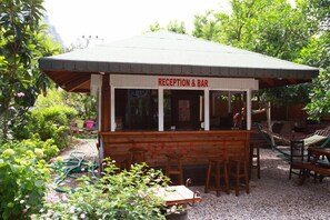 Zona de recepción y bar con muebles de madera y vistas al jardín.