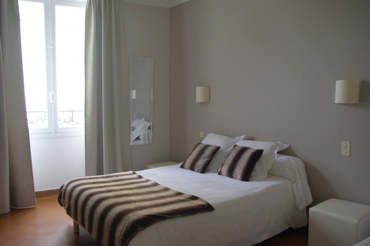 A bedroom with a bed, a nightstand, a lamp, and a window with curtains.