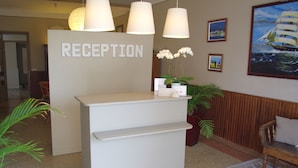 Un mostrador de recepción con un letrero que dice 'RECEPTION', una orquídea en maceta y cuadros en la pared.
