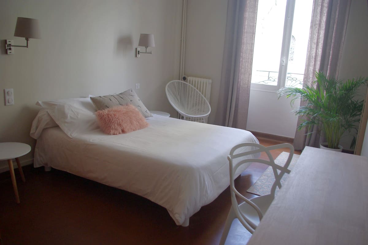A bedroom with a bed, a chair, a table, and a potted plant.