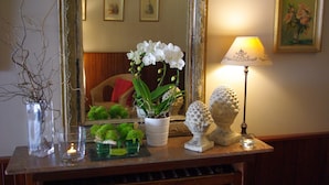 Una consola de madera con un espejo, una lámpara, un florero con orquídeas blancas y objetos decorativos.