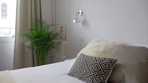 Un dormitorio ordenado con cama, una planta en maceta y una lámpara de pared.