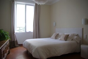 Une chambre à coucher avec un grand lit, une table de chevet, une commode et une fenêtre avec des rideaux.