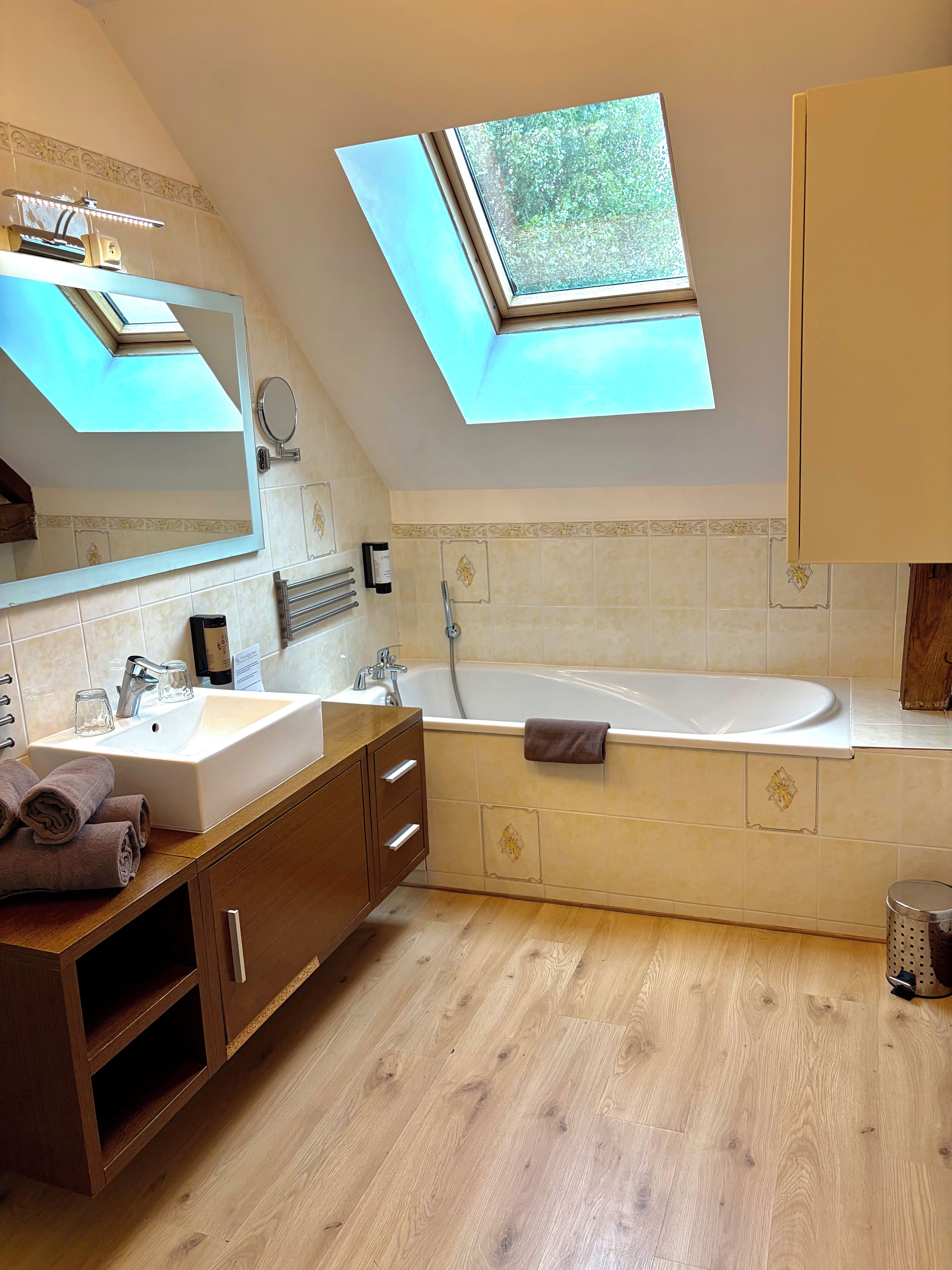 Une salle de bain moderne dotée d’une lucarne, d’une baignoire sur pieds et d’un meuble-lavabo avec un miroir.