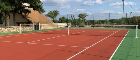 Cancha de tenis al aire libre con una red, rodeada de árboles y cielo despejado.