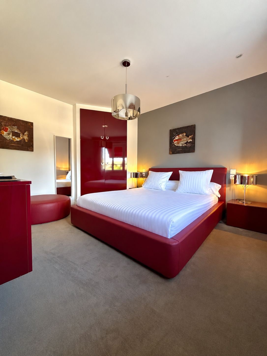 Une chambre moderne avec un grand lit, des touches de rouge et des œuvres d’art accrochées aux murs.