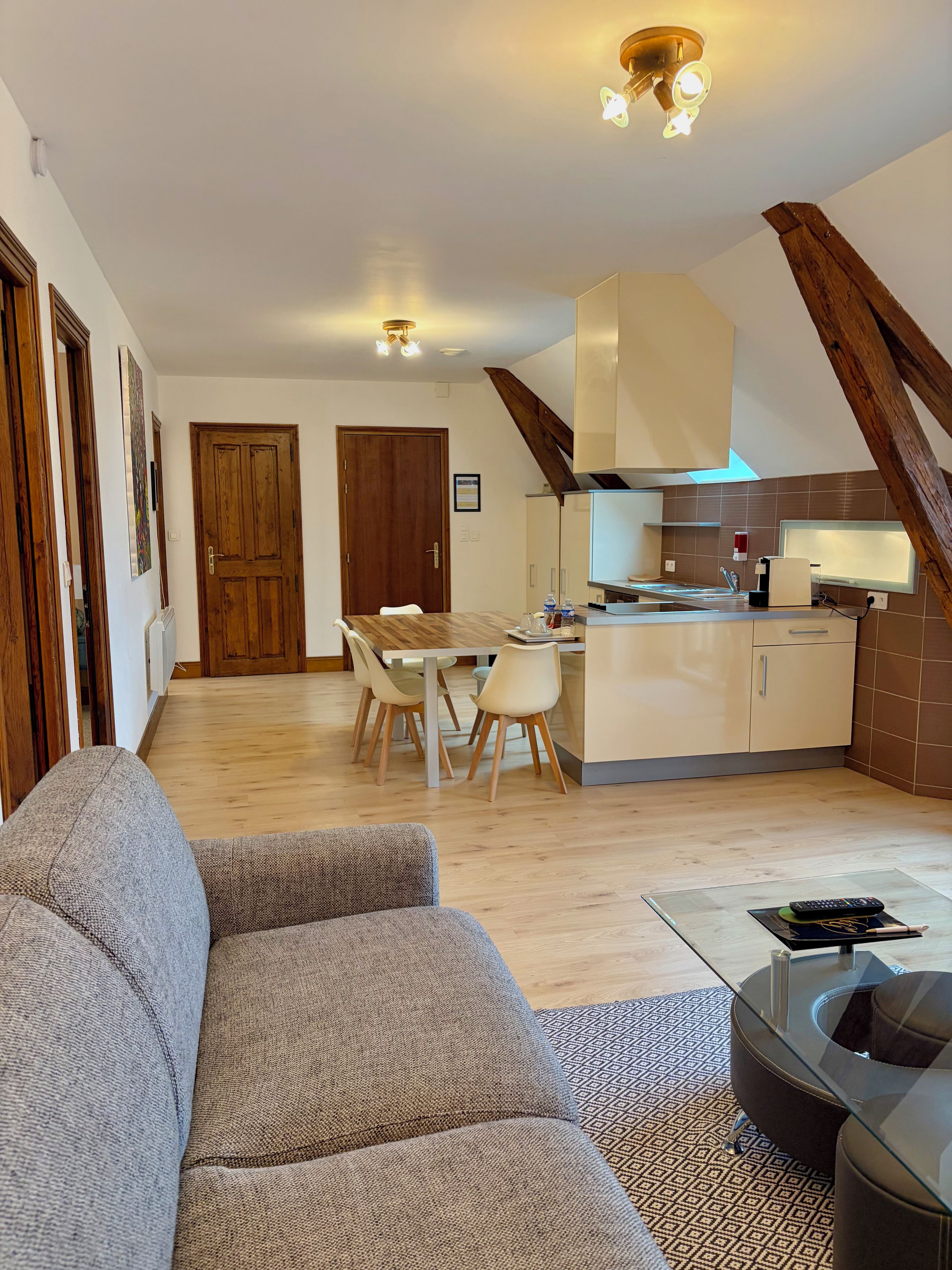 A modern kitchen with a dining area, wooden beams, and a sofa in the living room.