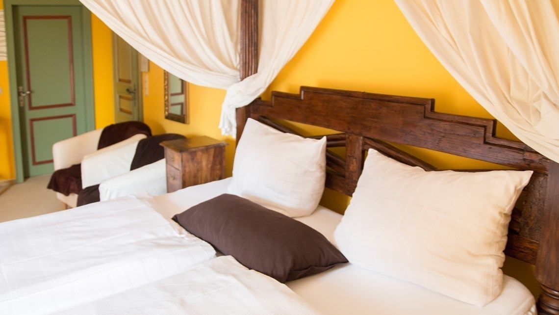 Ein Bett mit weißer und brauner Bettwäsche, ein Holz-Kopfbrett und eine grüne Tür im Hintergrund.