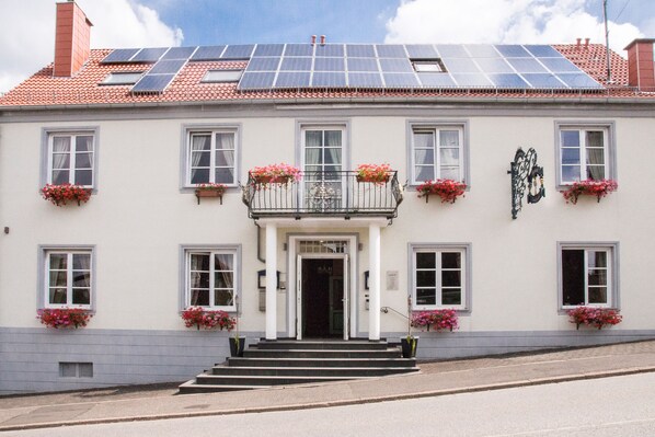 Un edificio con paneles solares en el techo, fachada blanca y varios balcones con macetas de flores.