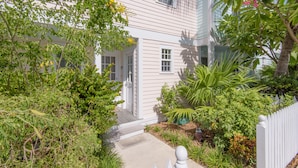 Een wit huis met een veranda, omringd door weelderige begroeiing en een witte picket fence.