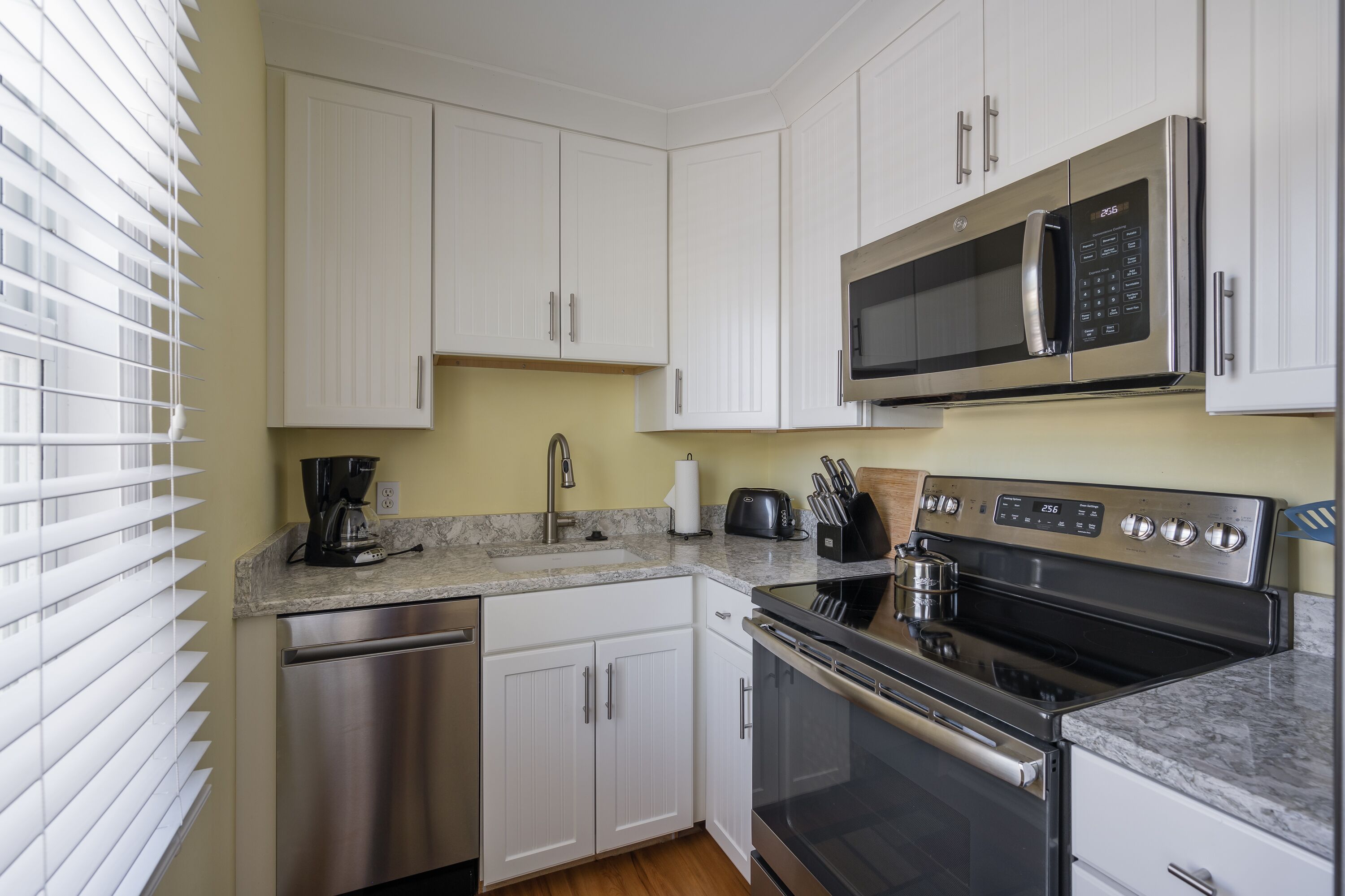 Una cocina moderna con armarios blancos, electrodomésticos de acero inoxidable, microondas, tostadora y lavavajillas.