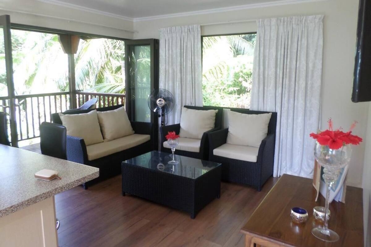 A room with a sofa set, a coffee table, a dining table, and a view of greenery outside.