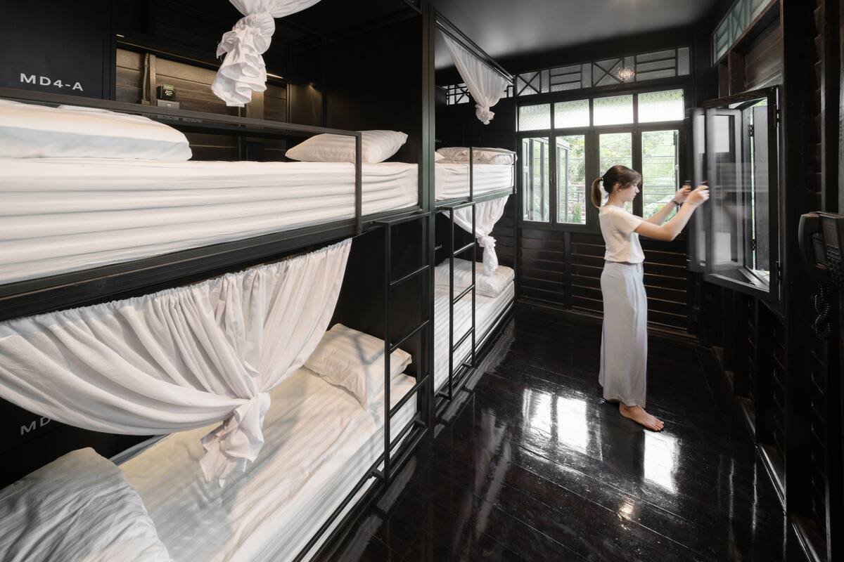 A hotel room with bunk beds, a large window, and a person adjusting the window blind.