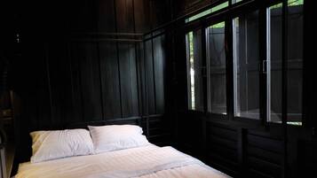 A dark wooden room with a bed, large windows, and a view of greenery outside.
