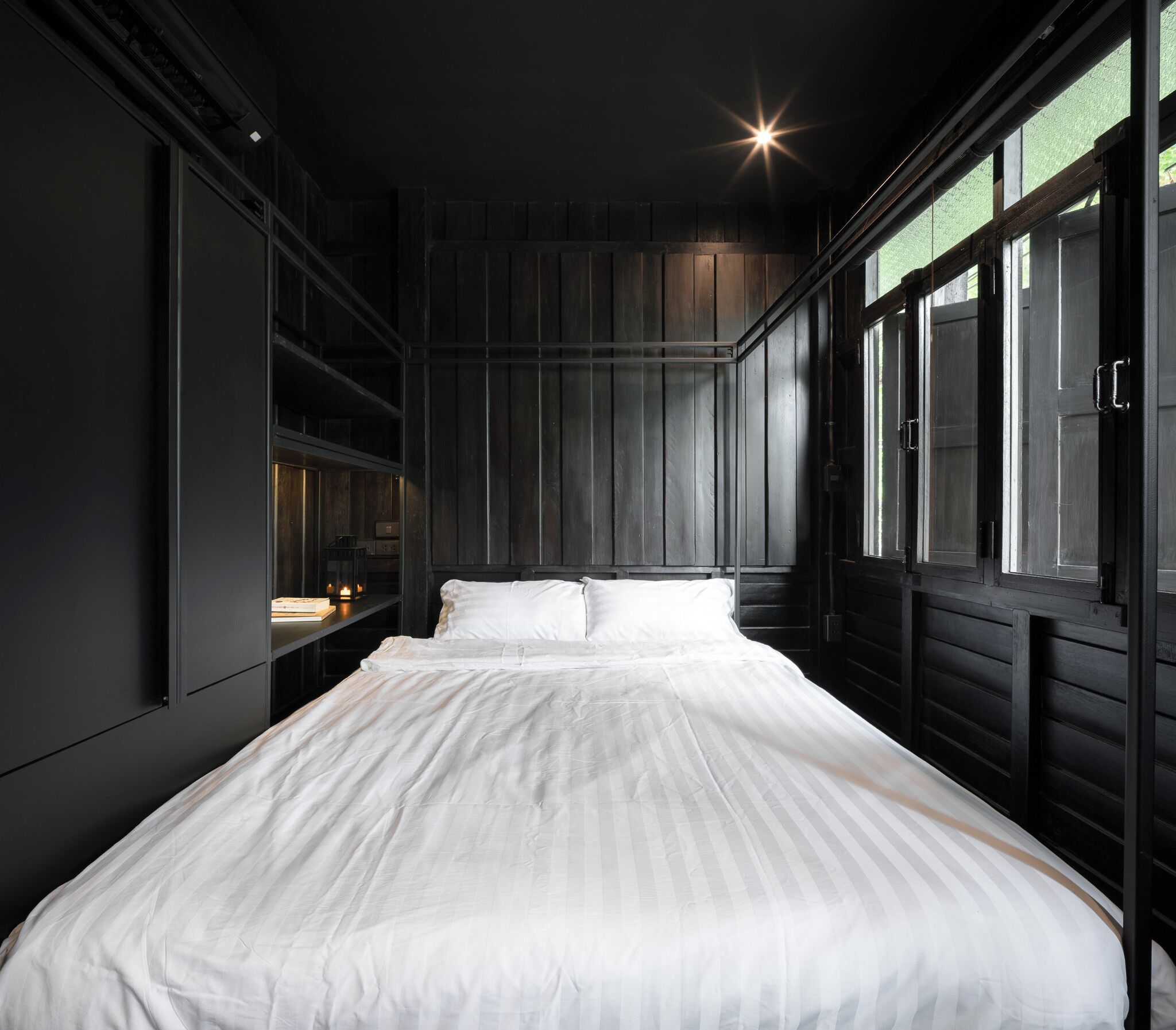 A modern bedroom with a large bed, dark wooden walls, and a window with a view.