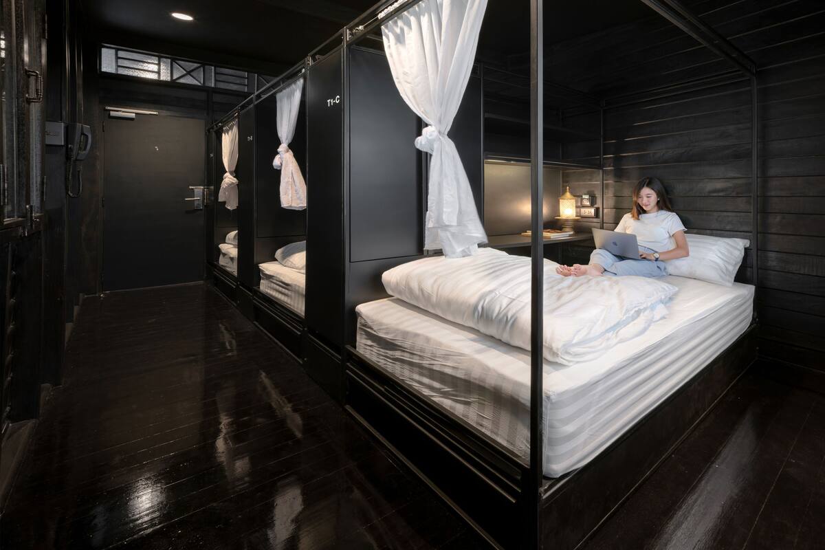 A modern hotel room with a four-poster bed, a bedside table with a lamp, and a phone.