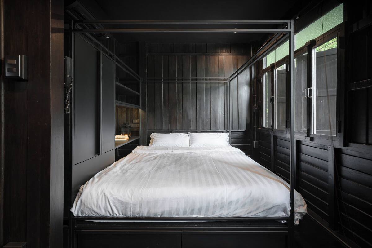 A single bed in a dark room with wooden walls and a window.