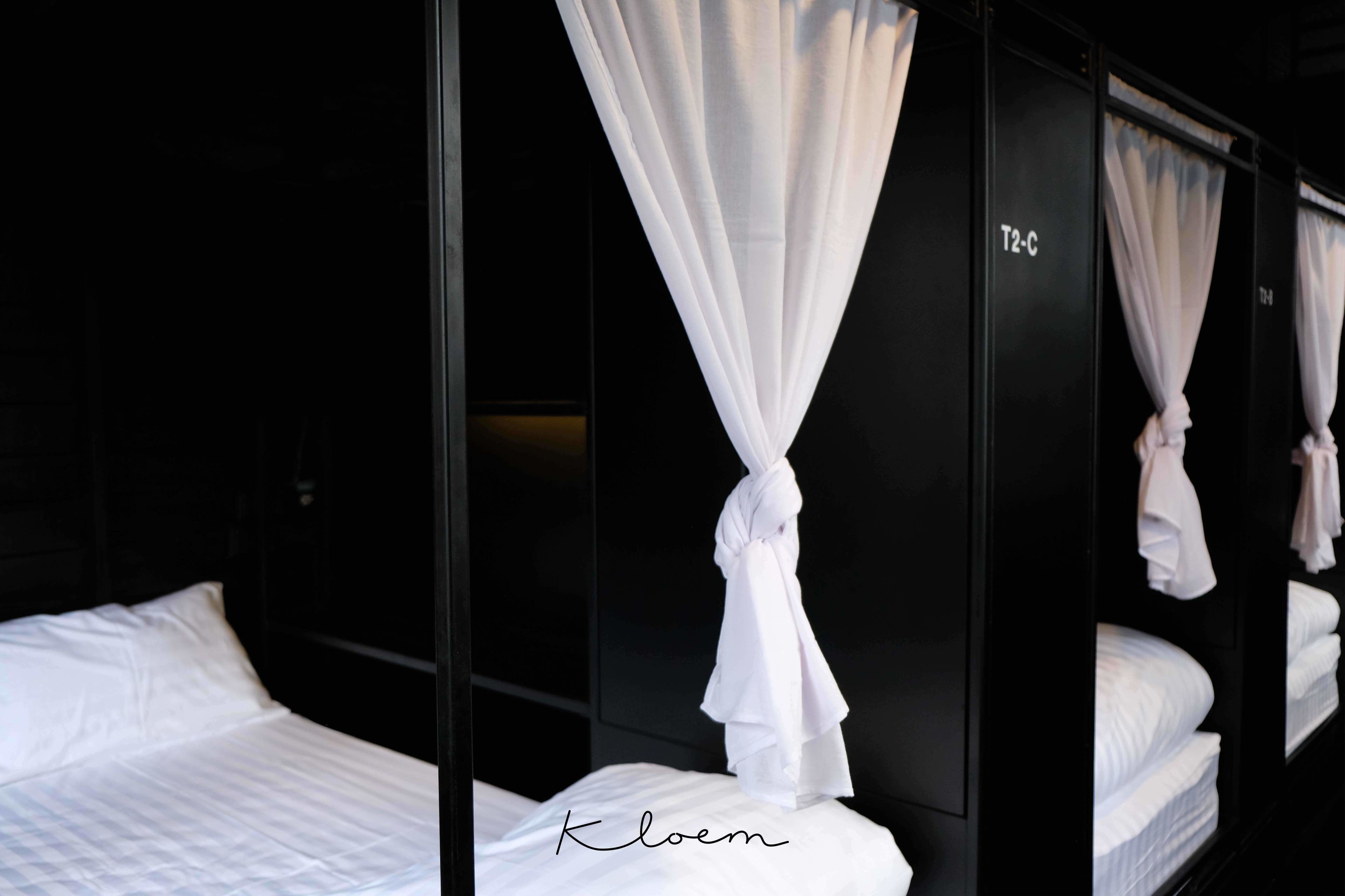 A hotel room with a bed, white curtains, and a black wardrobe.