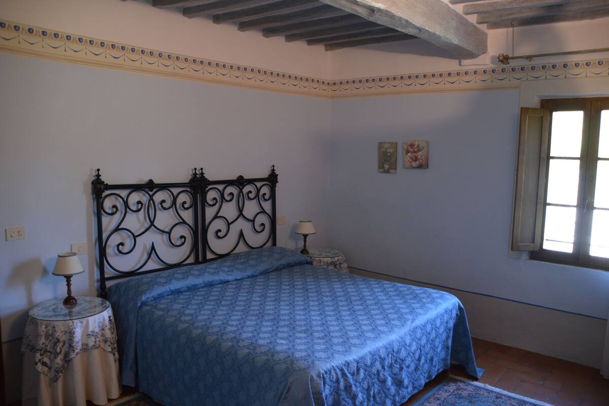 Un dormitorio con una cama, dos mesitas de noche con lámparas, una ventana y un detalle decorativo en el techo.