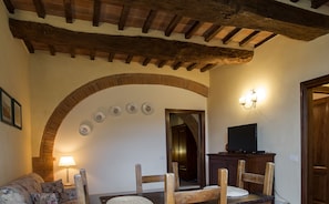 A cozy living room with a wooden ceiling, a fireplace, a television, and a dining area with chairs and a table. - Agriturismo Nobile (Montepulciano)