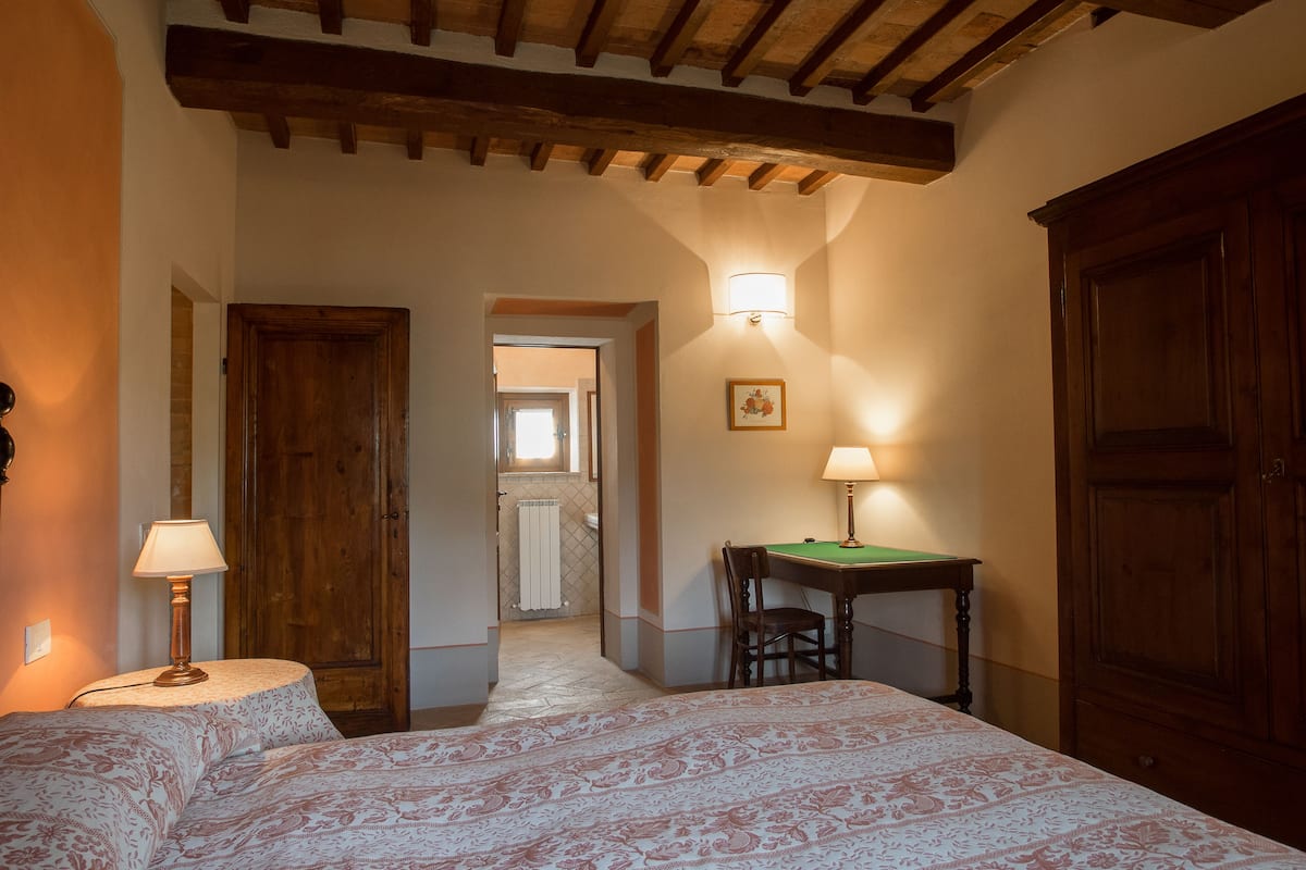 Un dormitorio con una cama, dos lámparas, una puerta de madera y una mesita.