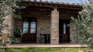 Un bâtiment en pierre avec un toit en tuiles, deux portes et un petit espace extérieur aménagé avec des chaises et des tables.