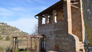 Un bâtiment rustique en pierre, doté d’une pergola en bois et offrant une vue sur une colline.