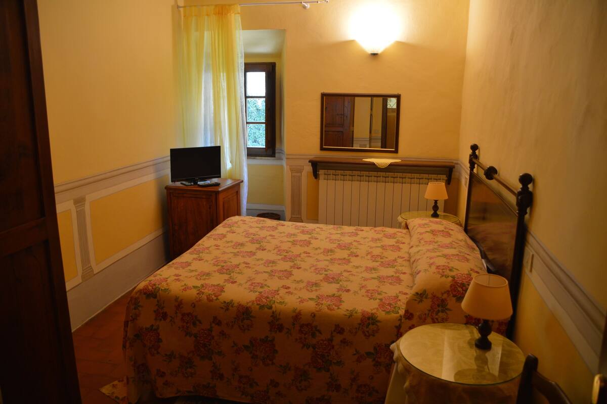 Un dormitorio con cama, televisión, lámpara y ventana con cortinas.