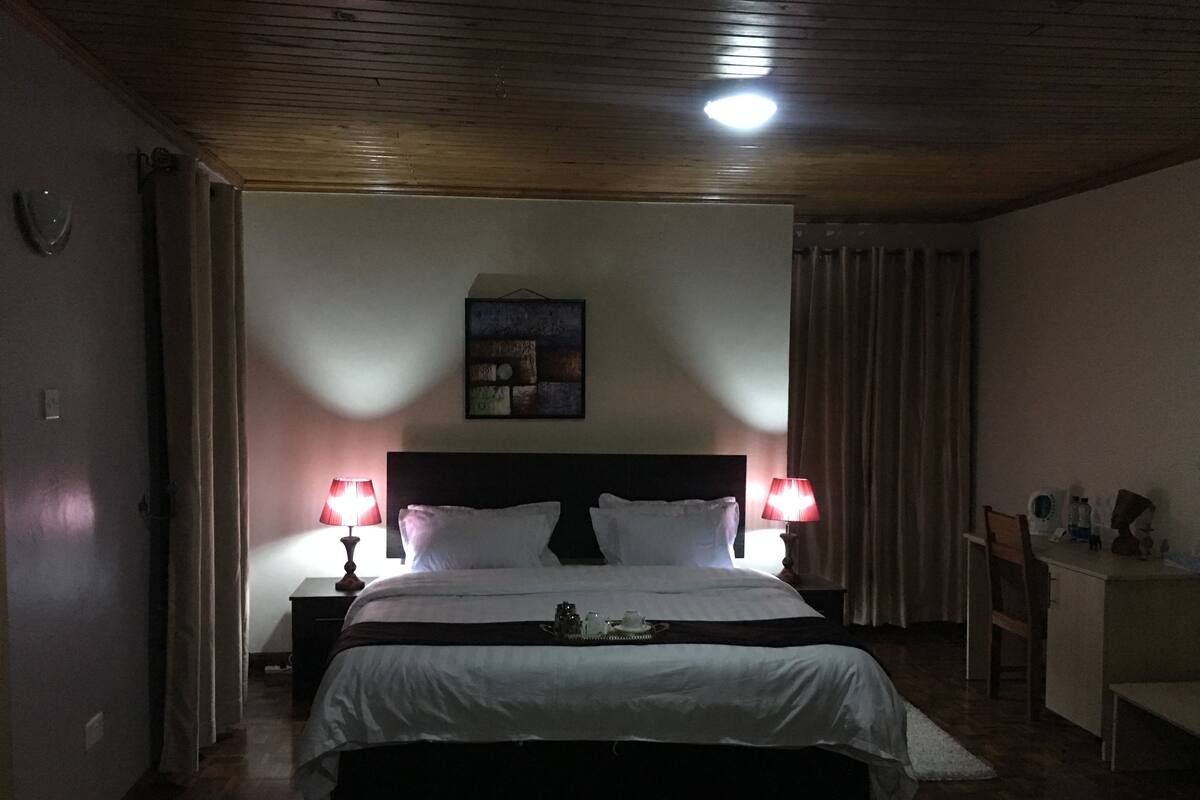 Un dormitorio con una cama grande, dos lámparas de noche, una mesita de noche, un escritorio con una silla y una lámpara de techo.