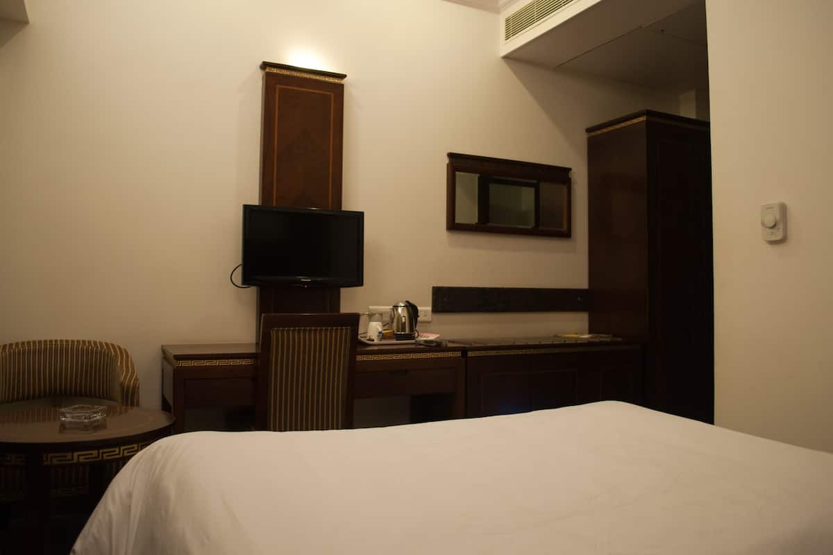 A hotel room with a bed, a television, a desk with a chair, and a cabinet.