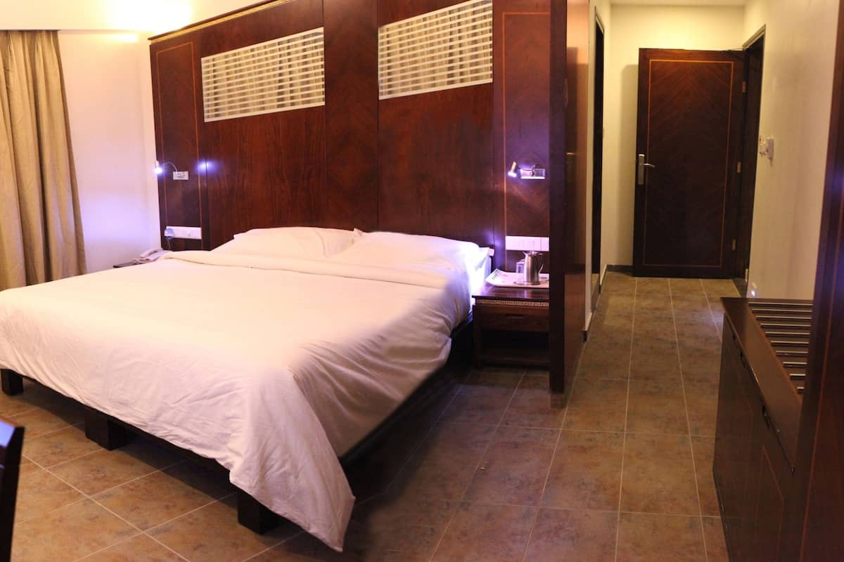 A hotel room with a large bed, a TV, a desk with a chair, and a bathroom door.