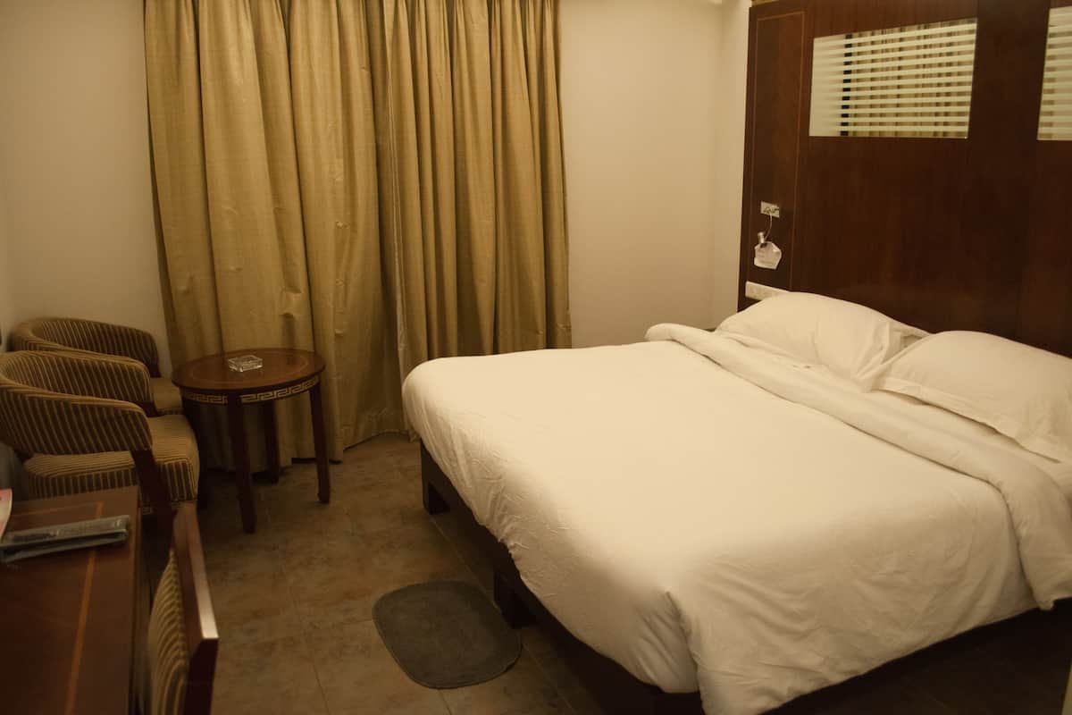 A hotel room with a bed, two chairs, a small round table, and a window with blinds.