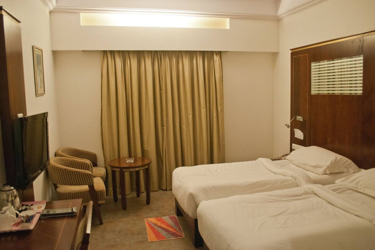A hotel room with two beds, a television, a small table, and a chair.