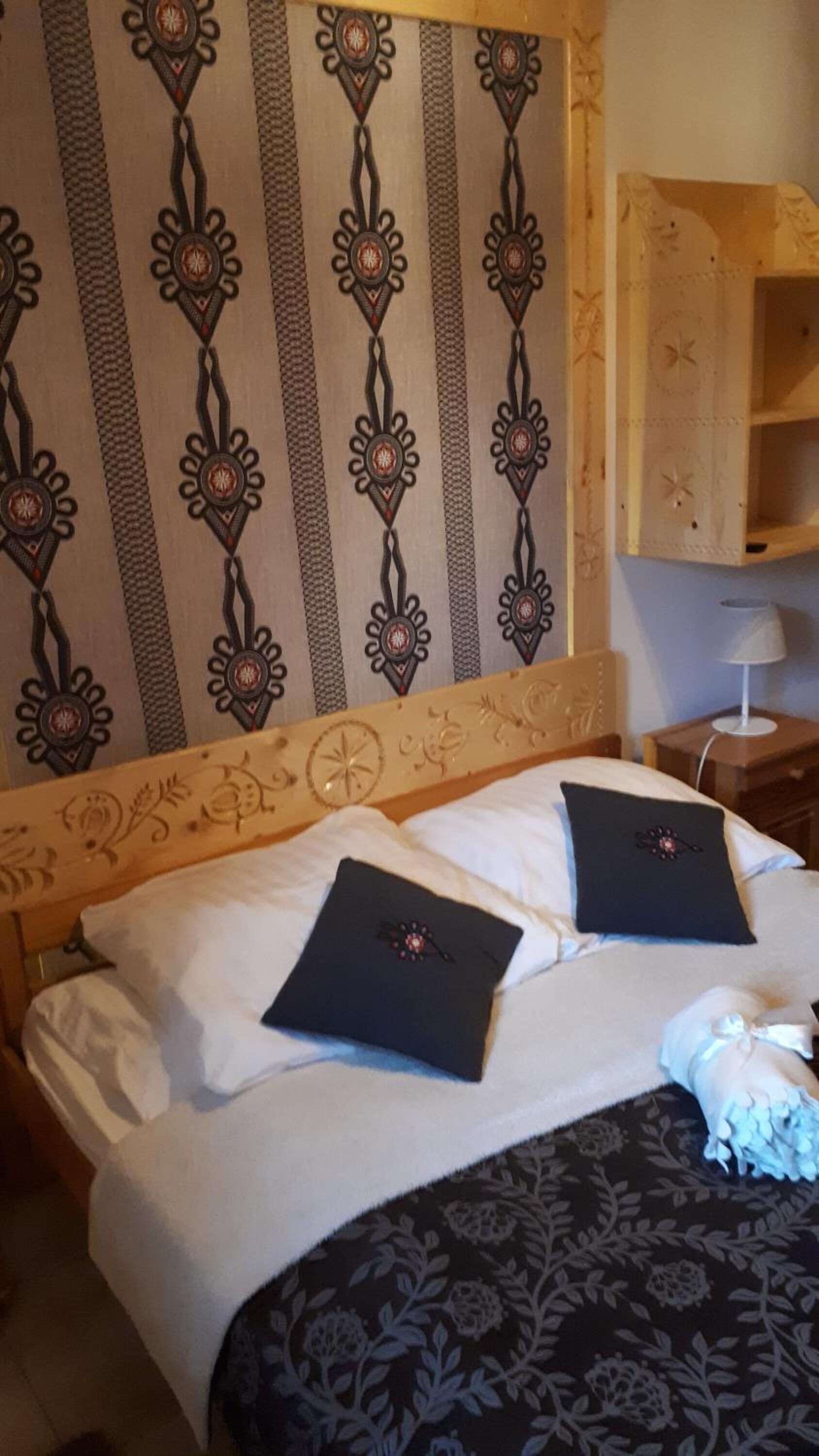 A neatly made bed with two black pillows, a patterned bedspread, and a headboard with decorative elements.