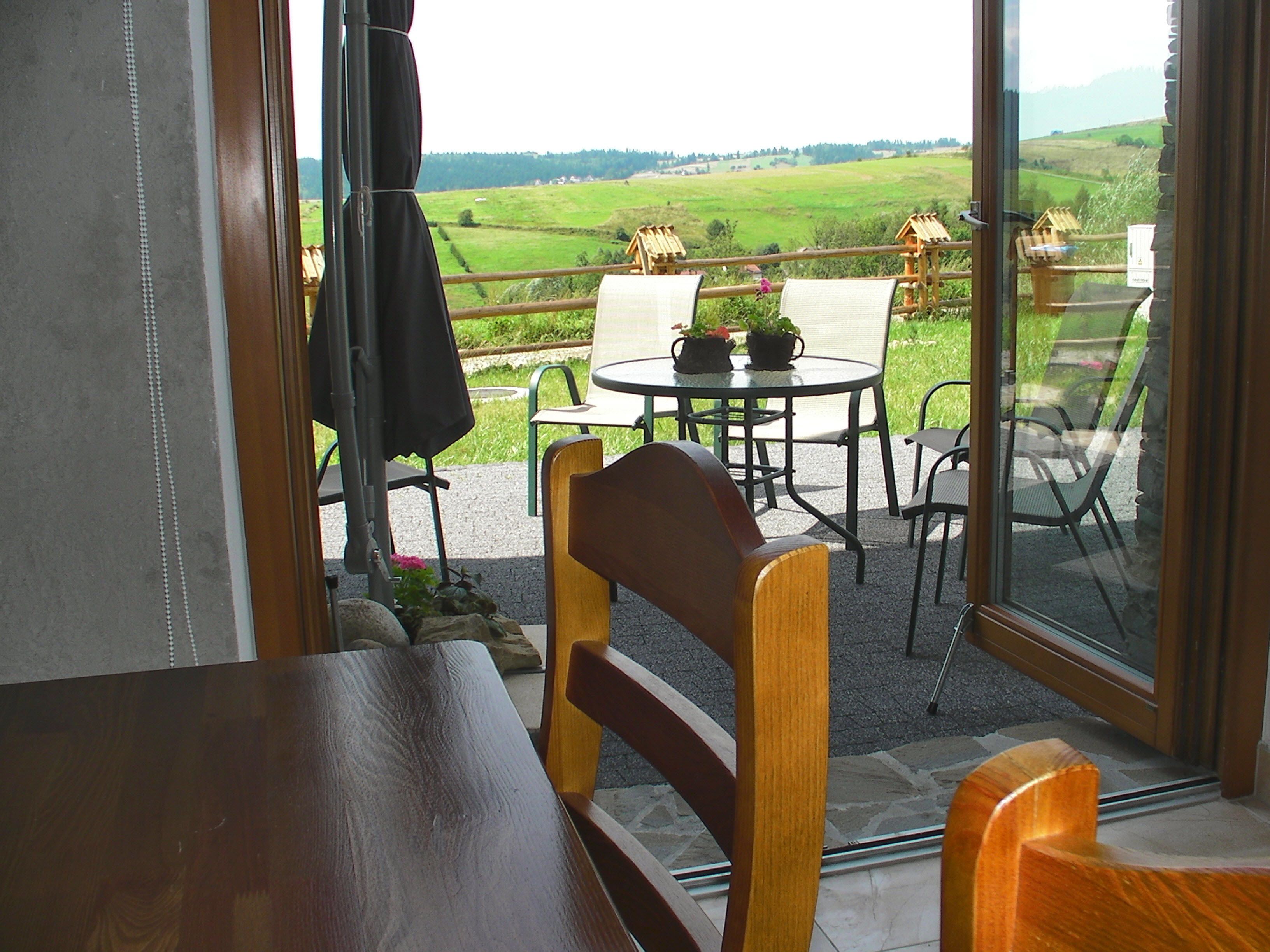 A room with a wooden bench, a table with chairs, and a view of a green field through a glass door.