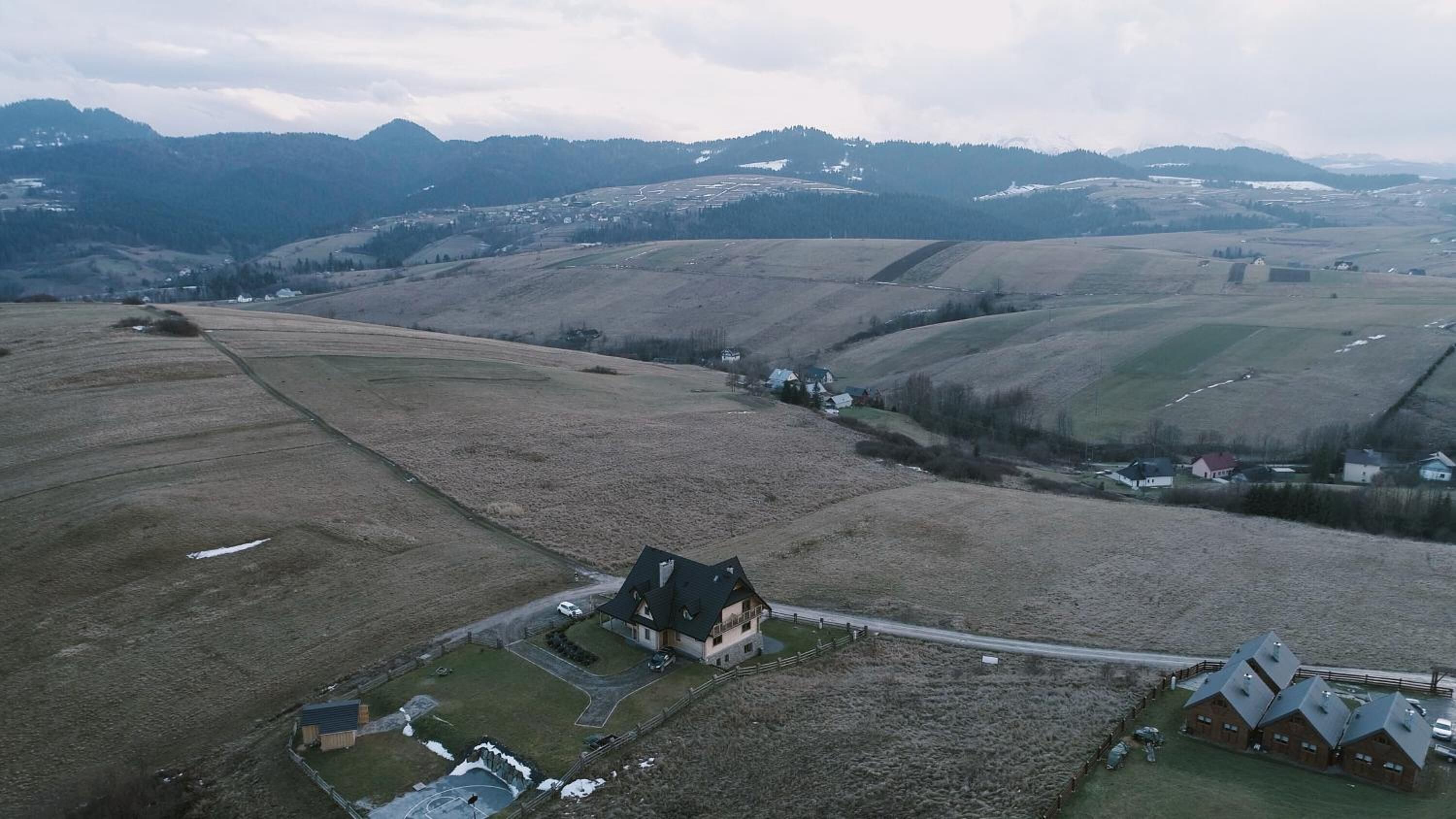 A rural landscape with rolling hills, a farmhouse, and a cluster of barns.