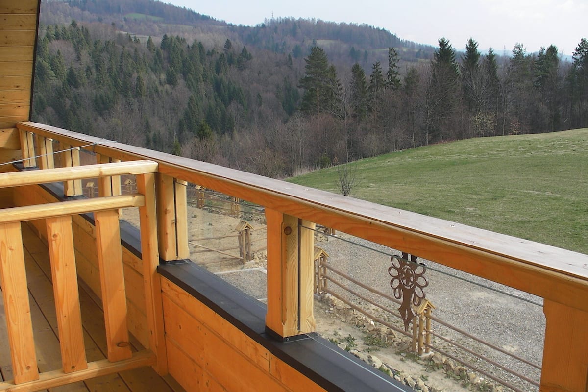 A wooden deck with a view of a forested hillside and a grassy field.