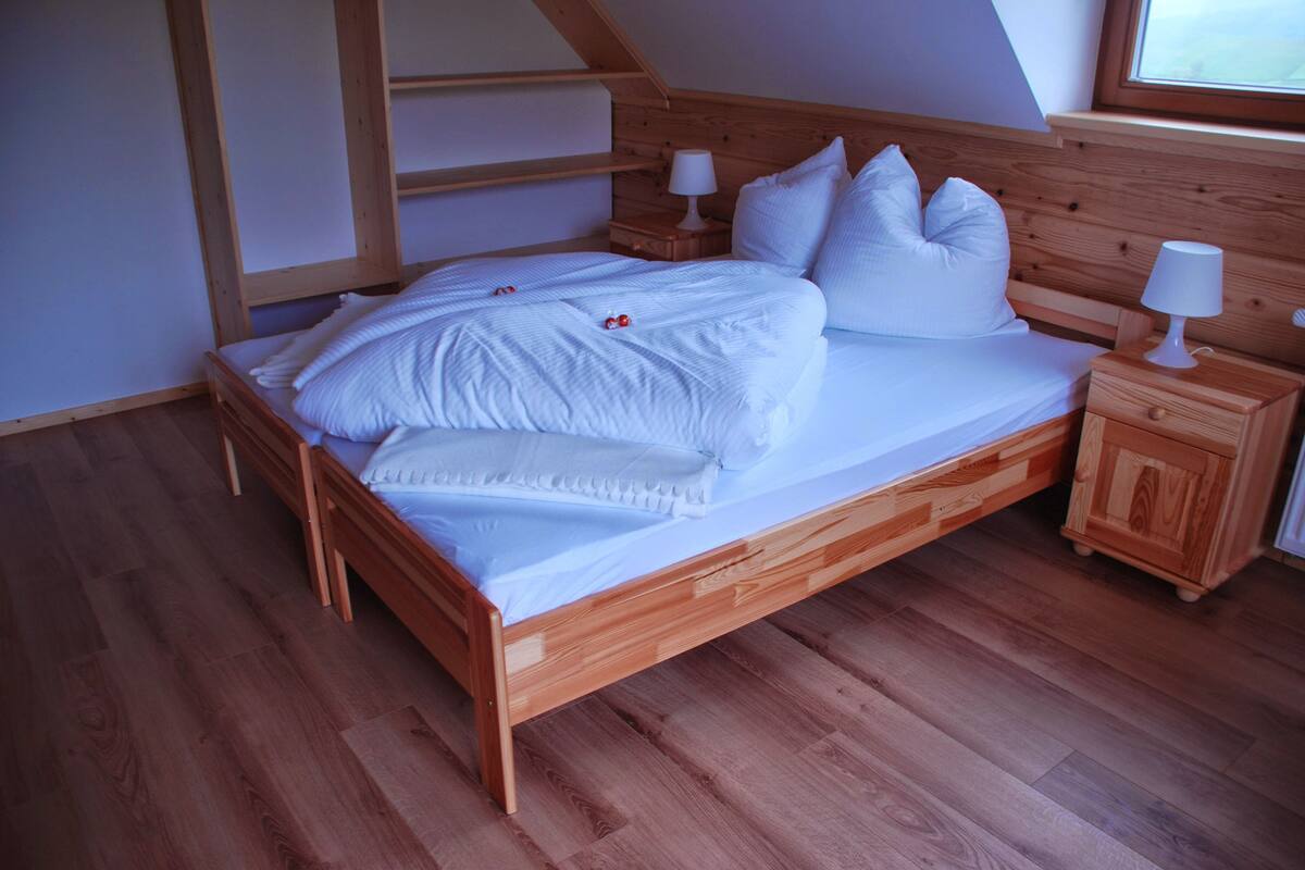 A wooden bed with white bedding and pillows, a nightstand with a lamp, and a wooden wardrobe.