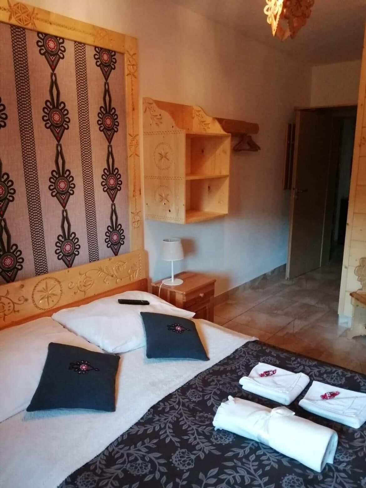 A hotel room with a bed, pillows, a nightstand, a lamp, and a wooden shelf.