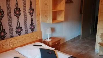 A hotel room with a bed, pillows, a nightstand, a lamp, and a wooden shelf.